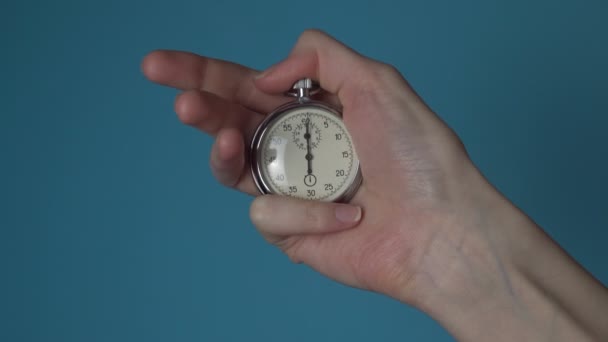 La mano de una mujer sostiene un cronómetro analógico en una pantalla cromakey azul. - Metraje, vídeo