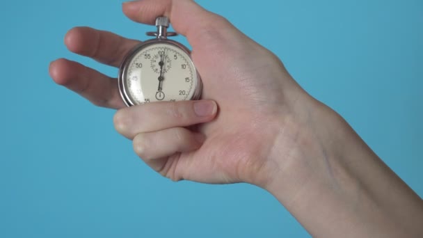 La mano de una mujer sostiene un cronómetro analógico en una pantalla cromakey azul. - Metraje, vídeo