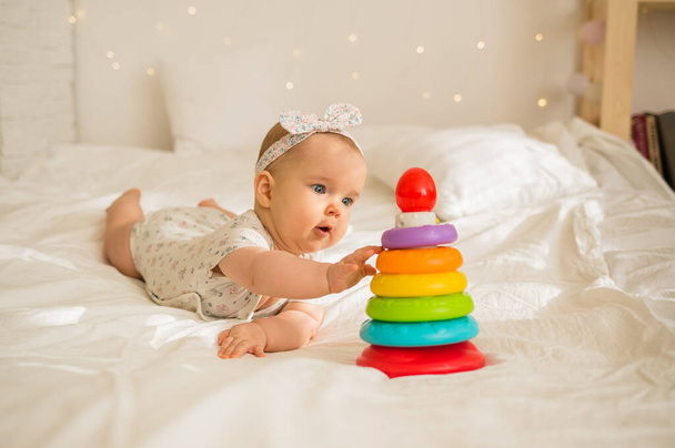 egy kislány színes öltönyben és fejpántban piramissal játszik egy fehér takarón az ágyon. - Fotó, kép