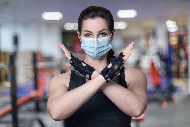 Mulher fitness em máscara mostra proibindo gesto com as mãos sobre fundo ginásio. - Foto, Imagem