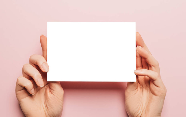 Female hands hold a blank sheet of paper on a pink background. Advertising space - Foto, immagini