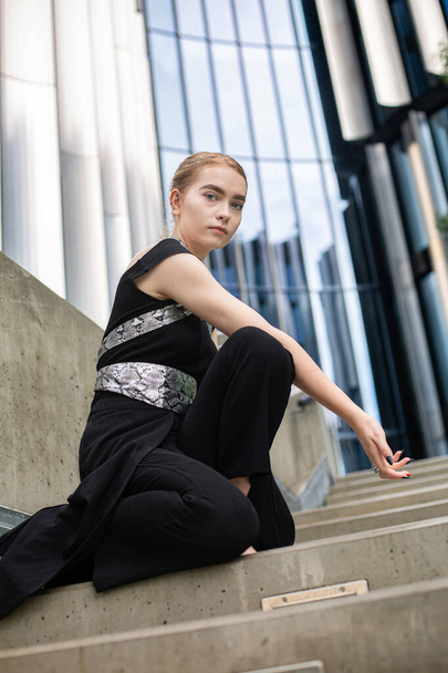 European young woman sitting on concrete stairs near metal panels - Valokuva, kuva