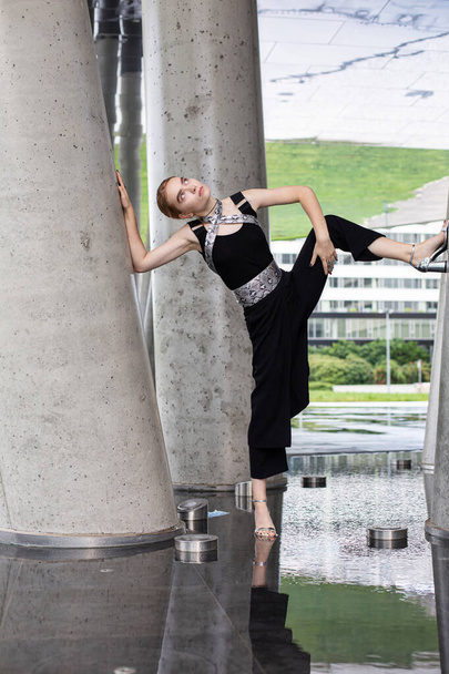 European young girl standing among concrete columns in black cocktail dress - 写真・画像