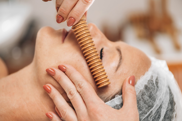 gezichtsmassage. Anti-aging madero therapie gezichtsbehandeling met geribbelde houten stok bij cosmetologie centrum  - Foto, afbeelding