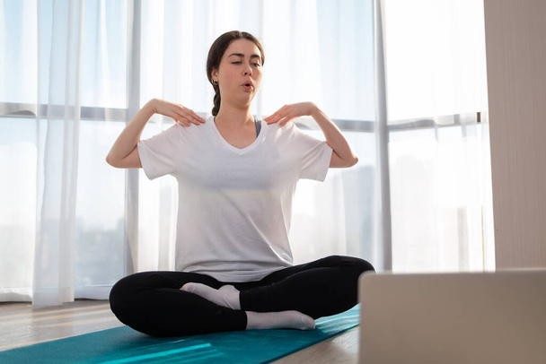 A young woman in sportswear, sitting doing yoga on online lessons. Indoor. Windows on the background. The concept of online training at home. - Foto, imagen