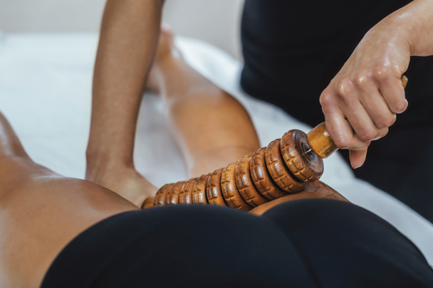 Masaje muscular de muslo posterior de terapia Madero con rodillo de madera o acorazado  - Foto, Imagen