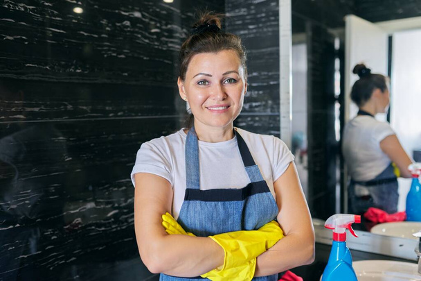 Portrait of middle-aged positive woman in apron gloves doing cleaning at home - Φωτογραφία, εικόνα