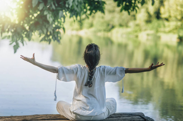 Meditace sebeobjevu v přírodě u jezera. Žena sedící v lotosové poloze medituje s otevřenou náručí  - Fotografie, Obrázek