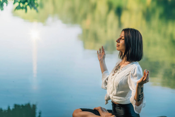 Retiro de meditação de ioga. Mulher sentada em posição de lótus com os dedos em Chin Mudra e meditando junto ao lago  - Foto, Imagem