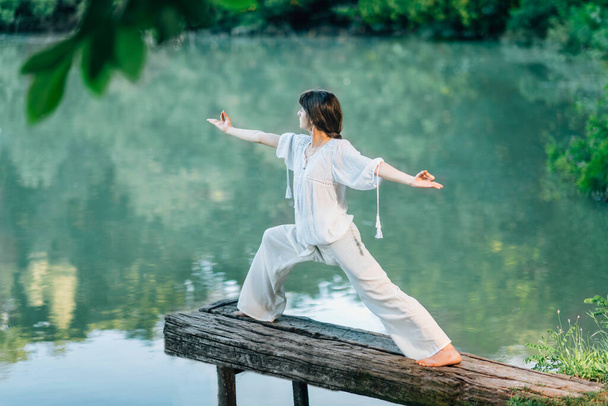 Yoga sul lago - Giovane donna che pratica Warrior 2 Pose o Virabhadrasana II - Foto, immagini