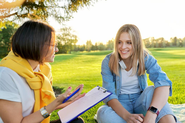 Rozmowa młodej kobiety z psychologiem, pracownikiem socjalnym, plenerem w parku na trawniku - Zdjęcie, obraz