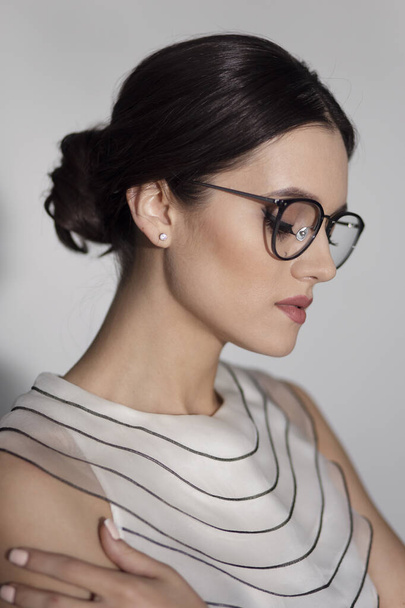 Retrato de perfil de cerca de una mujer elegante en gafas, aislada sobre un fondo gris. Vista vertical. - Foto, imagen