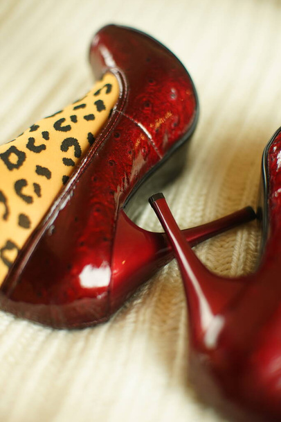 Női lábak leopárdharisnyában és vörös szabadalmaztatott magassarkúban fehér, puha kötött felületen. - Fotó, kép