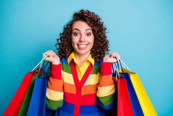 Photo of beautiful brown curly haired cheerful young woman raise shopping bag wonderful bargain isolated on blue color background - Fotó, kép