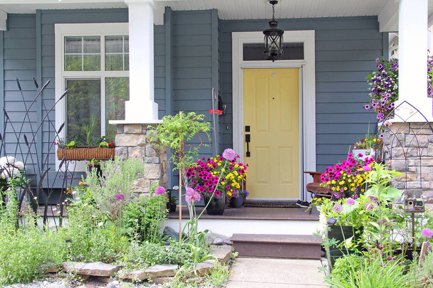 Желтая входная дверь маленького дома в пригороде Канады. Привлекательное и красочное крыльцо, окруженное многолетними и ежегодными цветами летом.  - Фото, изображение