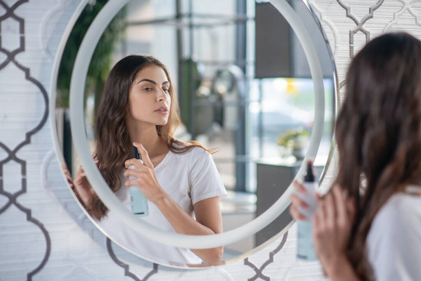 Woman using a hairspray near the mirror - Фото, зображення