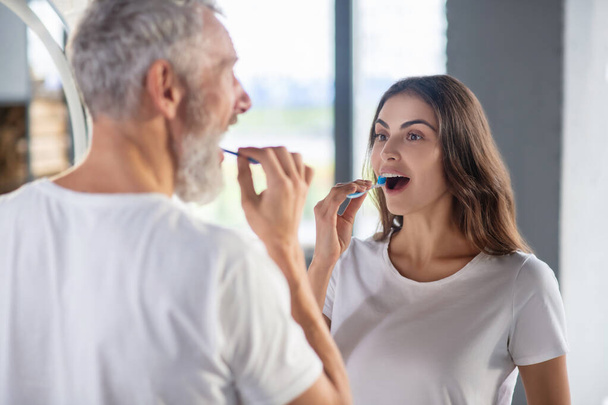 Woman and a man brushing their teeth together - 写真・画像