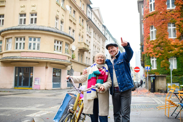 Happy senior couple with bicycle outdoors on street in city. - Φωτογραφία, εικόνα