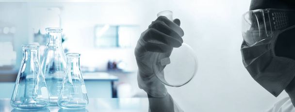 scienziato con occhiali di protezione guanti e maschera in possesso di fiaschetta in scienza medica laboratorio sfondo blu banner  - Foto, immagini