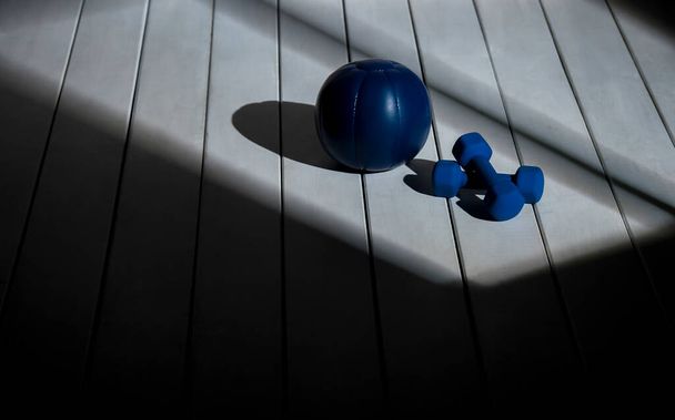 Balle de médecine bleue et haltères bleues sur le sol en bois. Concept du sport à domicile - Photo, image