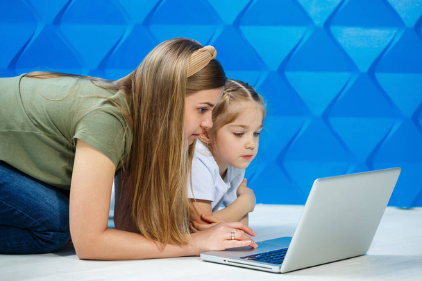Schattig klein meisje op zoek klaar om de laptop toetsenbord te gebruiken terwijl zitten op de keukenvloer met haar liefhebbende moeder - Foto, afbeelding