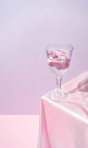 Champagne glass filled with flower petals on table with pink silk fabric. Minimal modern still life. Mother day and Valentines day concept background design. - 写真・画像