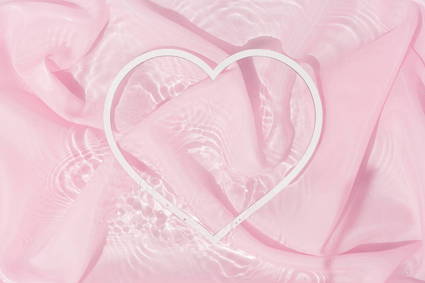 Herzförmige Dekoration im Wasser mit Seidenstoff. Valentinstag und Frauentag Hintergrunddesign. Minimal flache Lagen. - Foto, Bild