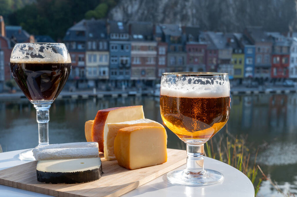 Drinking of dark and strong Belgian abbey beer with cheeses in sunny day with nice view on Maas river and town Dinant, Belgium - Photo, Image