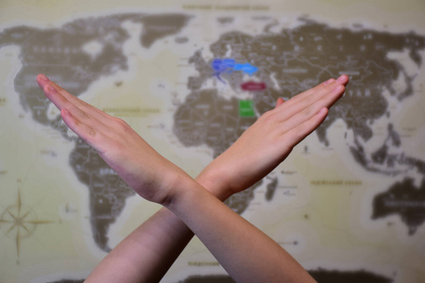 Due mani umane incrociate in un cartello proibitivo di fronte a una mappa del mondo con uno sfondo molto sfocato - Foto, immagini