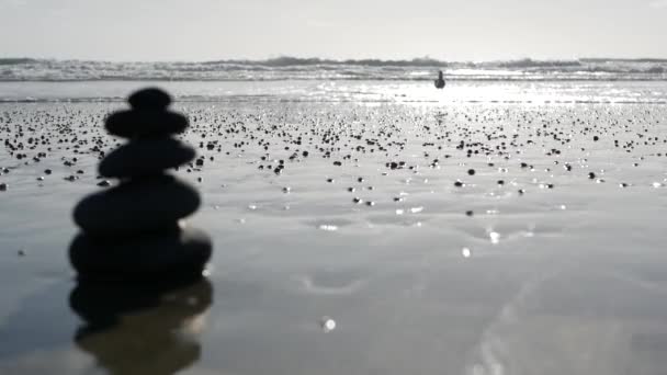 Ροκ εξισορρόπηση στην παραλία του ωκεανού, πέτρες στοίβαγμα από κύματα θαλασσινού νερού. Πυραμίδα βότσαλου στην αμμώδη ακτή - Πλάνα, βίντεο
