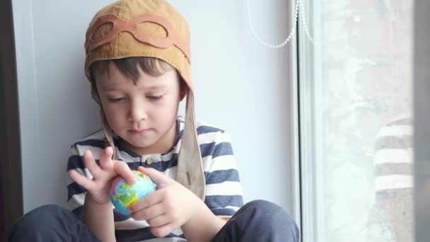 Litille serious boy in helmet with glasses playing with globe. Dream trawel - Footage, Video