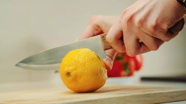 Hands with knife cutting lemon on the kitchen board - Foto, Imagen