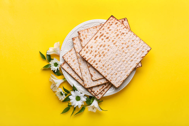 Plate with Jewish flatbread matza for Passover and flowers on color background - Photo, Image