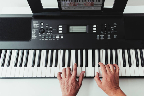 Vista superior de las manos de un hombre en un teclado de piano junto a una tableta con una aplicación de lección de piano. Concepto de lecciones de música en línea - Foto, imagen