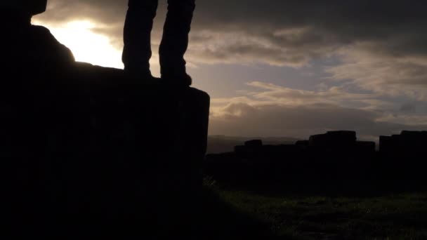 Vrouw springt van rotsen tegen zonsondergang en wolken  - Video
