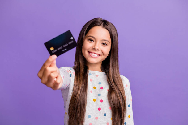Photo portrait of smiling little girl with long brunette hair showing blurred debit card isolated on bright purple color background - Foto, Bild