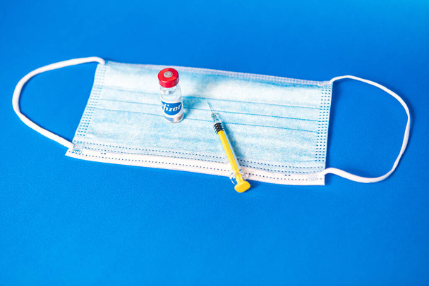 MADRID, SPAIN - JAN, 25, 2021: Vial with Pfizer company logo filled with Covid-19 vaccine, surgical mask and syringe on blue background. - Photo, Image
