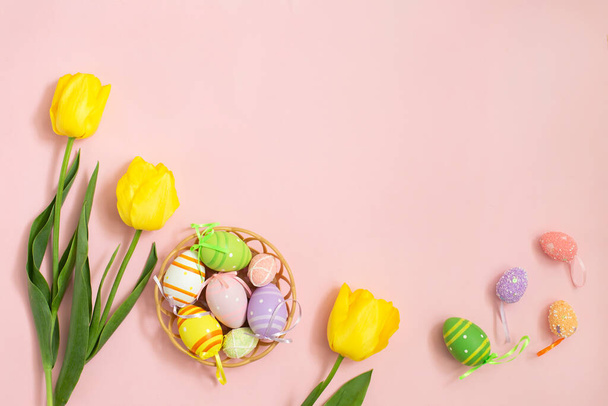Χρώμα πασχαλινά αυγά και άσπρες κίτρινες τουλίπες σε ροζ φόντο. - Φωτογραφία, εικόνα