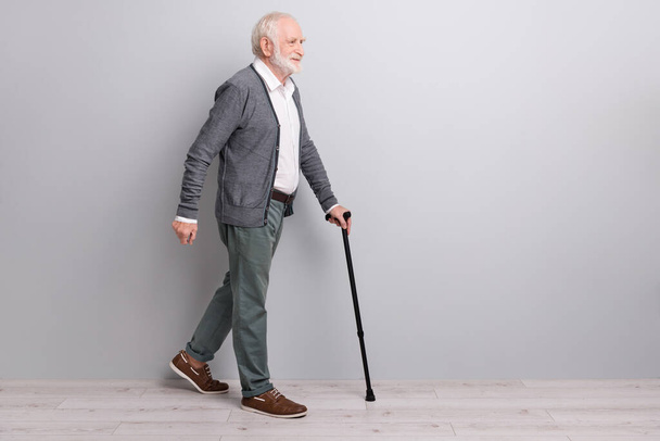 Full size profile photo of old man go with wand wear dark sweater trousers isolated on grey wall - Foto, Imagen