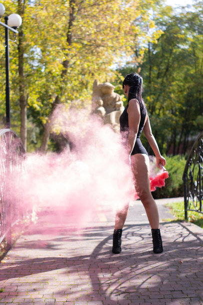 нерозпізнана струнка дівчина брюнетка в чорному костюмі з яскраво-рожевою димовою бомбою. танцює, розважається. кольоровий порошок. весна, літо, осінь. Високоякісна фотографія
 - Фото, зображення