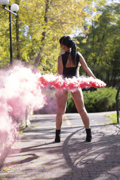 brunette fille mince méconnaissable en costume noir avec bombe de fumée rose vif. danser, s'amuser. poudre de couleur. printemps, été, automne. Photo de haute qualité - Photo, image