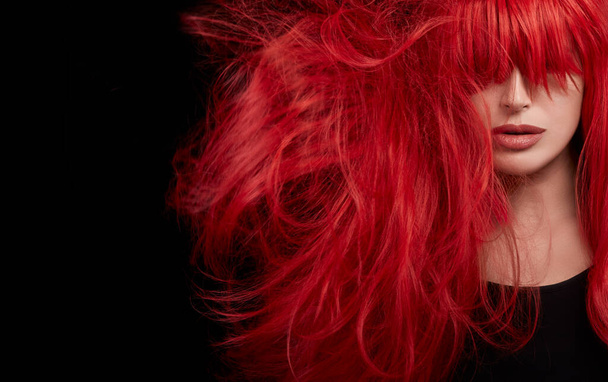 Genç bir kadın uzun ve parlak saçlarını sallıyor. Profesyonel kızıl saç rengine boyanmış. Siyah arkaplanda izole edilmiş yakın plan portresi - Fotoğraf, Görsel