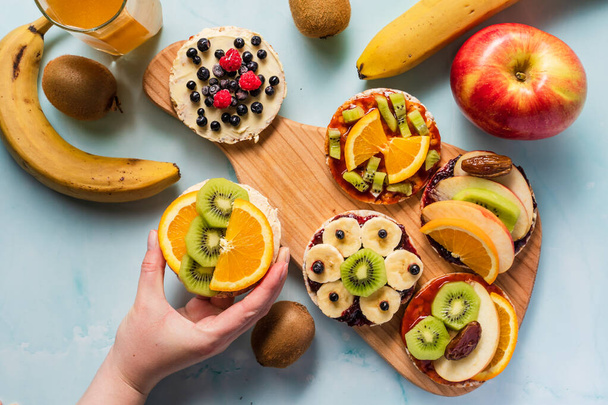 Křupavé rýžové koláčky na stole s čerstvým ovocem kiwi banán jablečné borůvky maliny a pomeranč na stole - horní pohled na ruce, přičemž zdravé organické vegetariánské nebo veganské snídaně bezlepkové - Fotografie, Obrázek