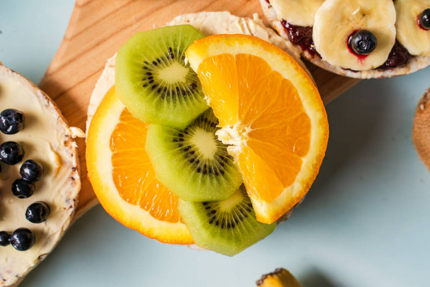 Pasteles de arroz inflados crujientes en la mesa con kiwi de fruta fresca de plátano y naranja en la mesa - vista superior en saludable vegetariano orgánico o desayuno vegano sin gluten - Foto, imagen
