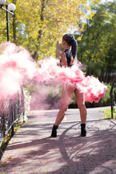 irreconocible chica delgada morena en body negro con bomba de humo de color rosa brillante. bailando, divirtiéndose. polvo de color. primavera, verano, otoño. Foto de alta calidad - Foto, Imagen