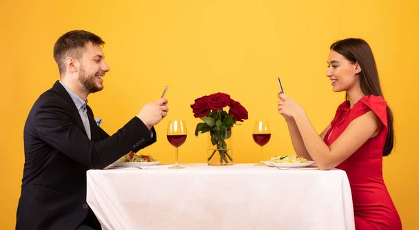 Ευτυχισμένο ζευγάρι χρησιμοποιώντας Smartphones κατά τη διάρκεια ρομαντικό δείπνο, κίτρινο φόντο, Πανόραμα - Φωτογραφία, εικόνα