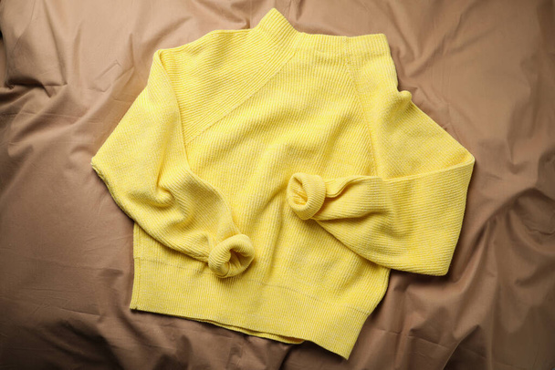 Beautiful yellow warm sweater on brown bedsheet, top view - Φωτογραφία, εικόνα