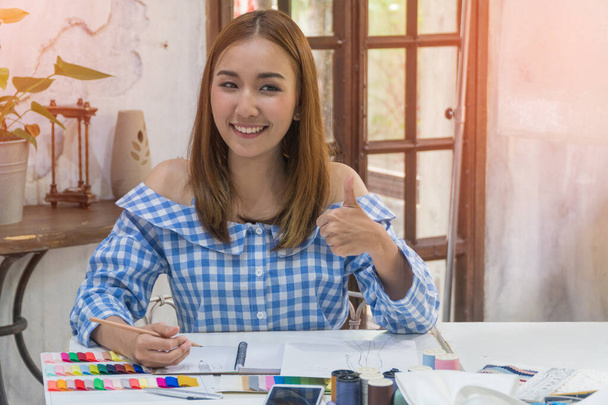 азиатская женщина портниха или дизайнер большие пальцы вверх и счастливо улыбается с швейными аксессуарами. - Фото, изображение
