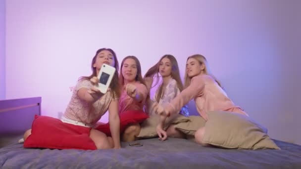 Cuatro hermosas mujeres jóvenes felices en pijama se sienta en la cama, canta y graba vídeo en sus teléfonos en la despedida de soltera - Metraje, vídeo