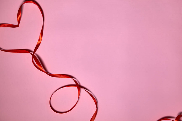 Серце з червоної стрічки на рожевому тлі, вид зверху. Святкова прикраса. Стрічка у формі серця. Вітальна листівка на день Святого Валентина
 - Фото, зображення